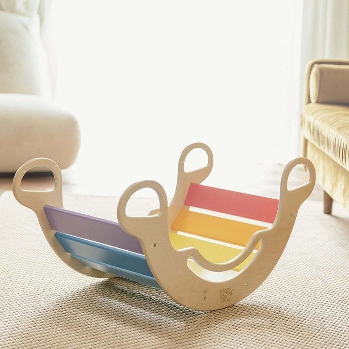 Colorful wooden sandbox in the shape of a duck, with sections in purple, blue, yellow, and pink, on a beige carpet in a living room.