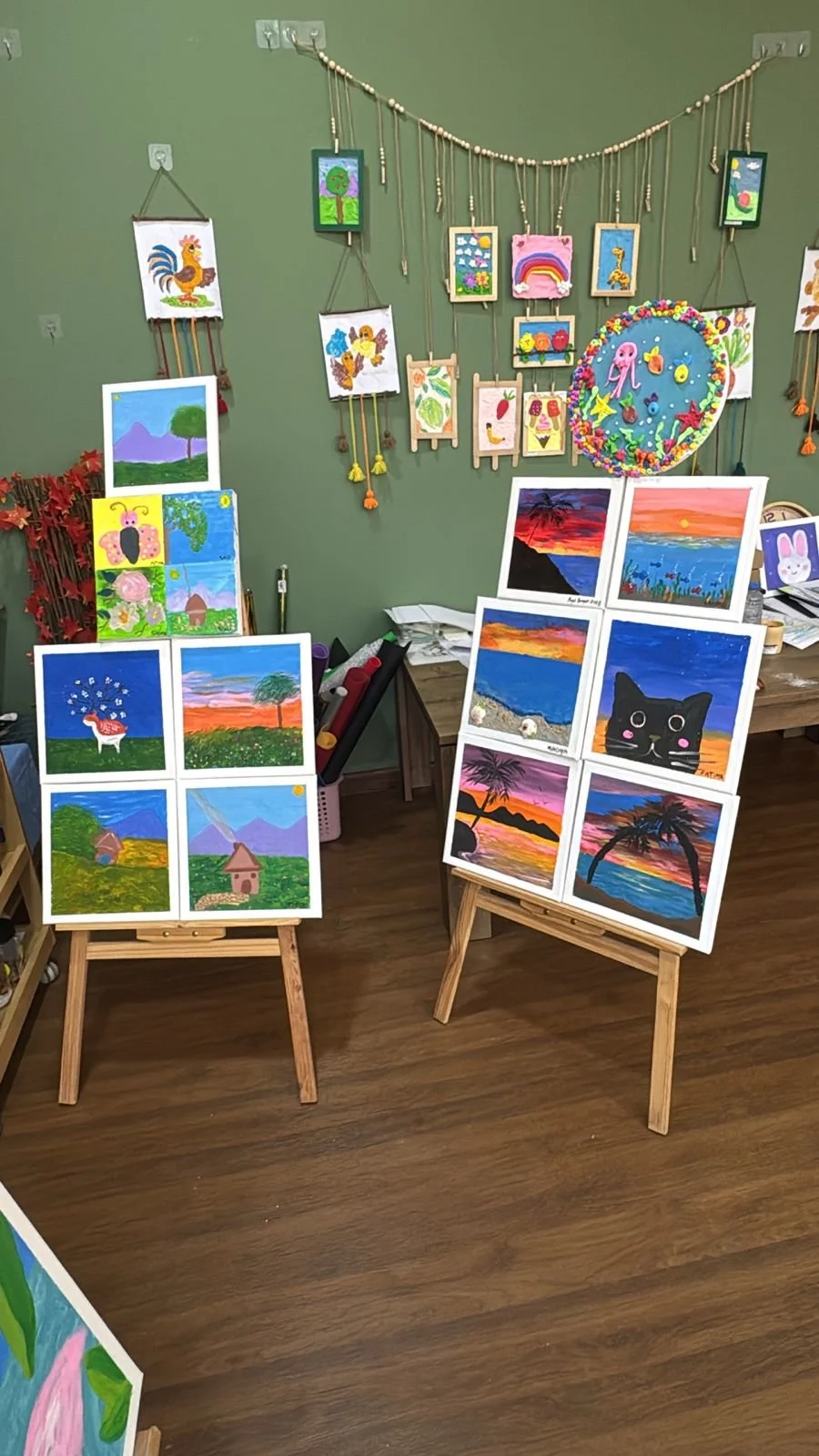 Art display with colorful paintings of landscapes, animals, and abstract scenes on easels and walls in a room.