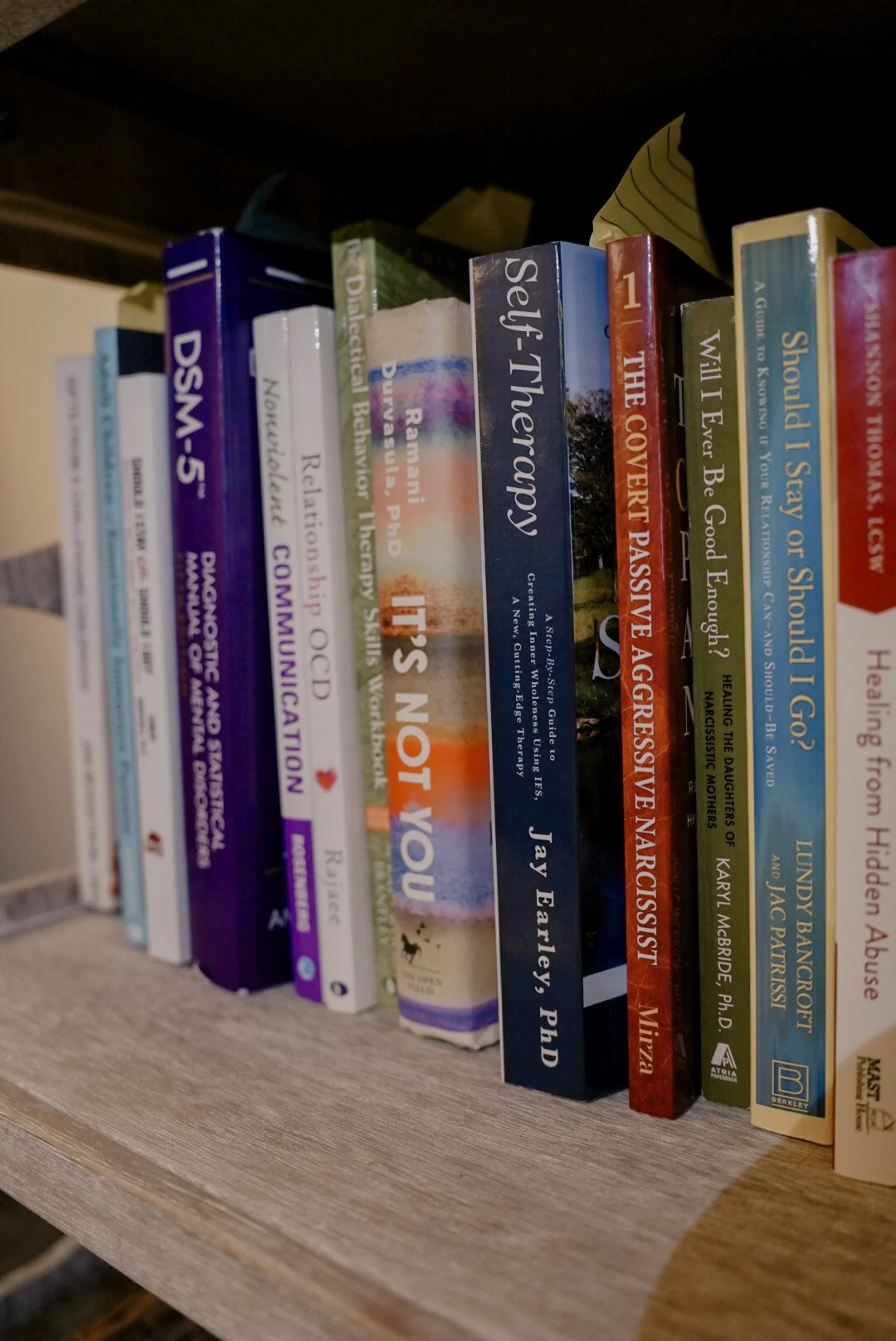 A close-up of a bookshelf with various books, including titles on self-help, health, and relationships, arranged vertically.