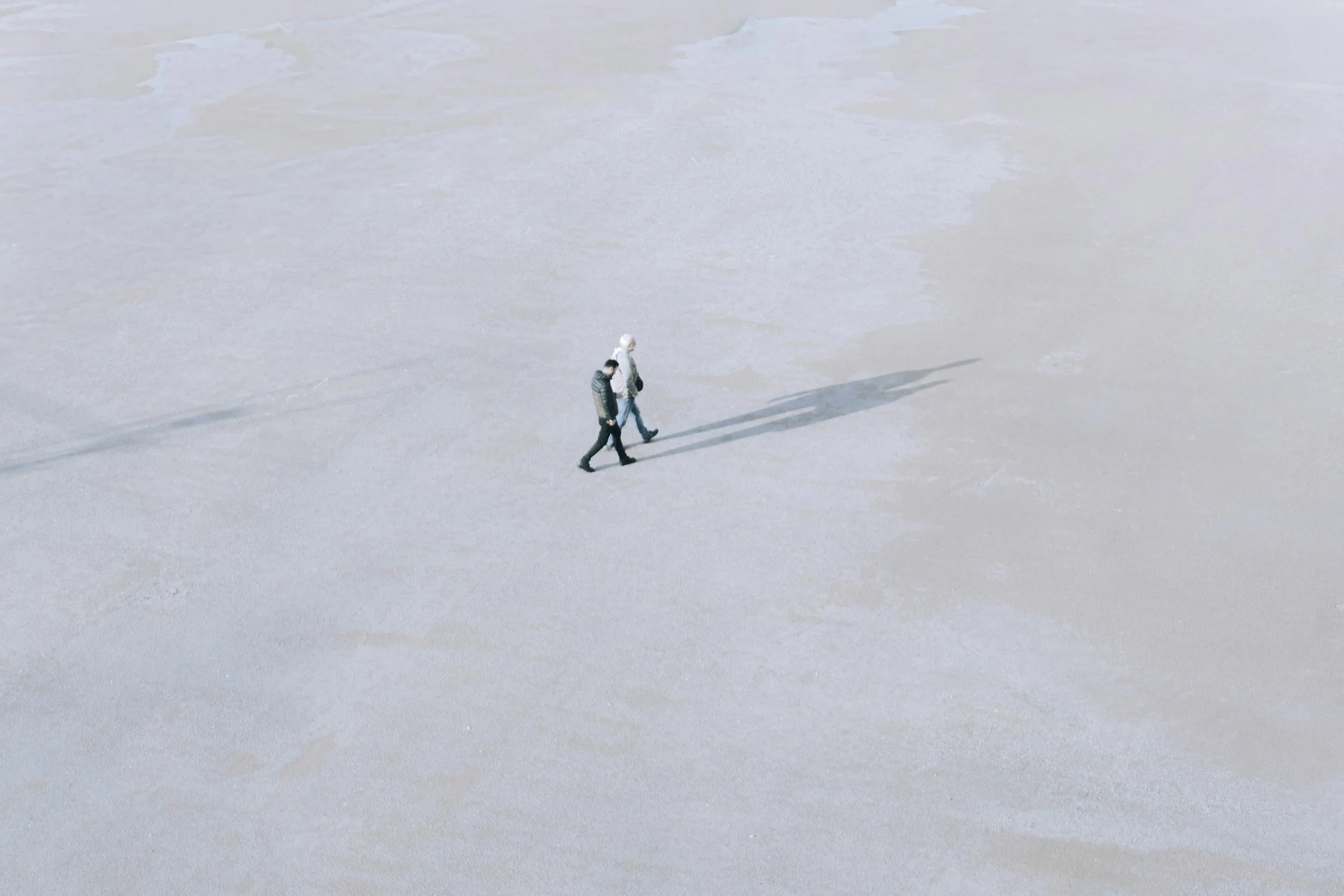 Two people walking on a vast, empty desert with long shadows.
