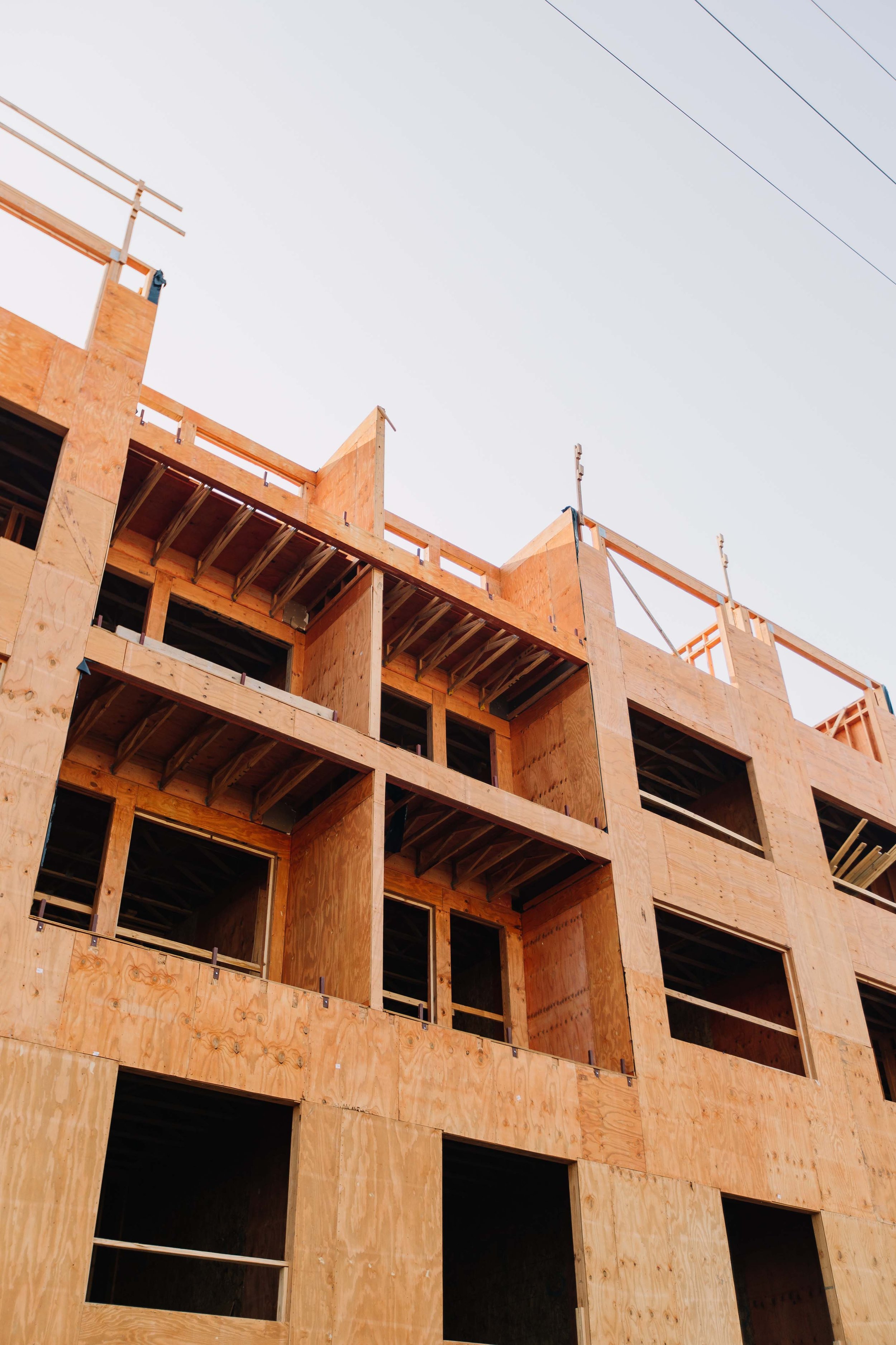 A multi-story building under construction, with wooden framework and open spaces for windows or doors, and power lines in the sky above.