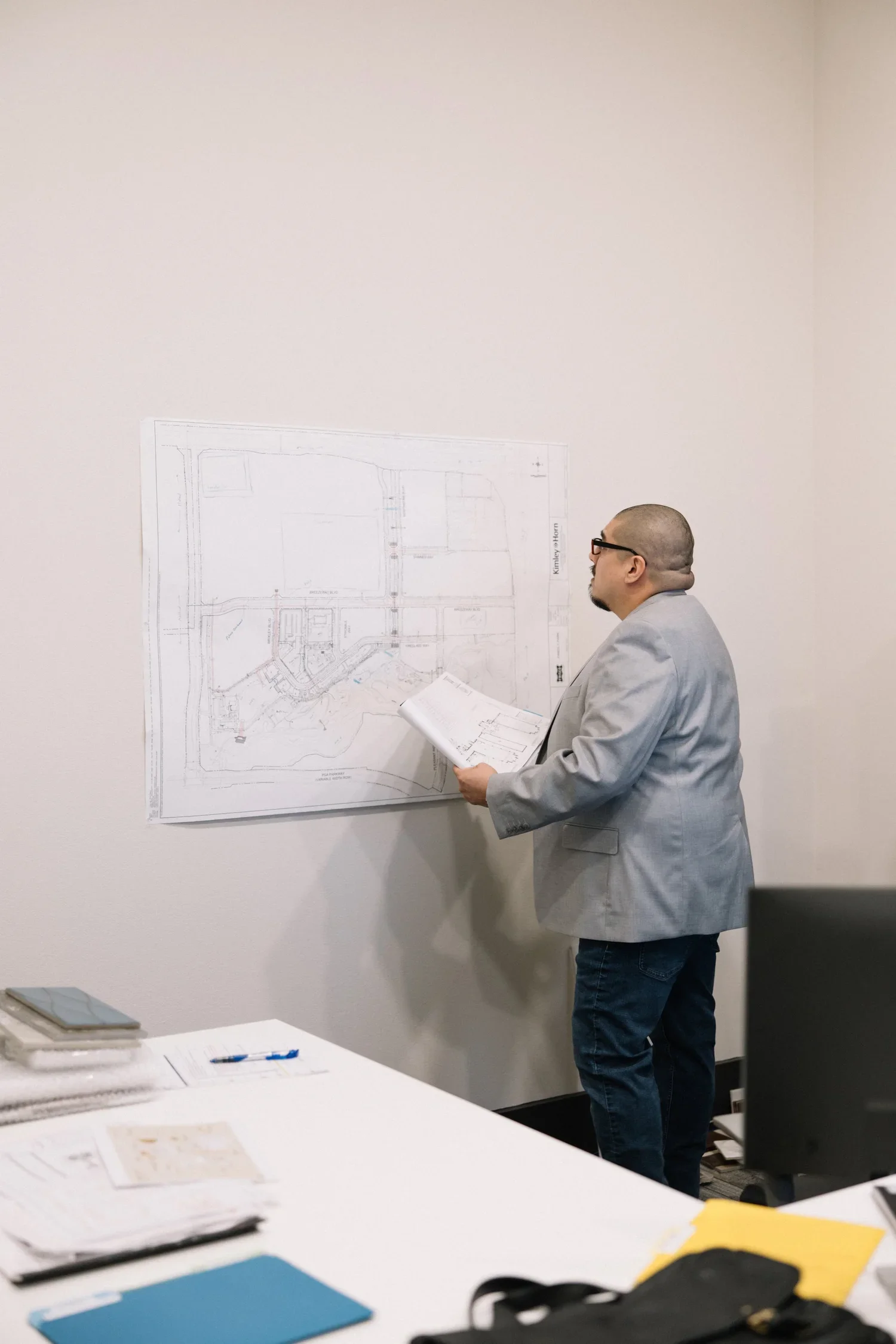 Man in glasses wearing a gray blazer looking at architectural plans on wall.