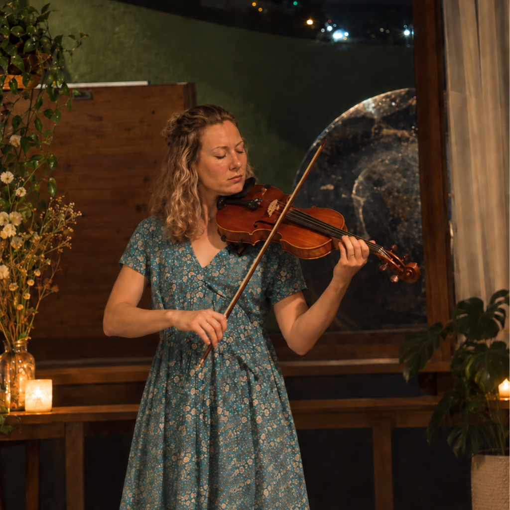 A woman playing the violin in an indoor setting with candles and plants.