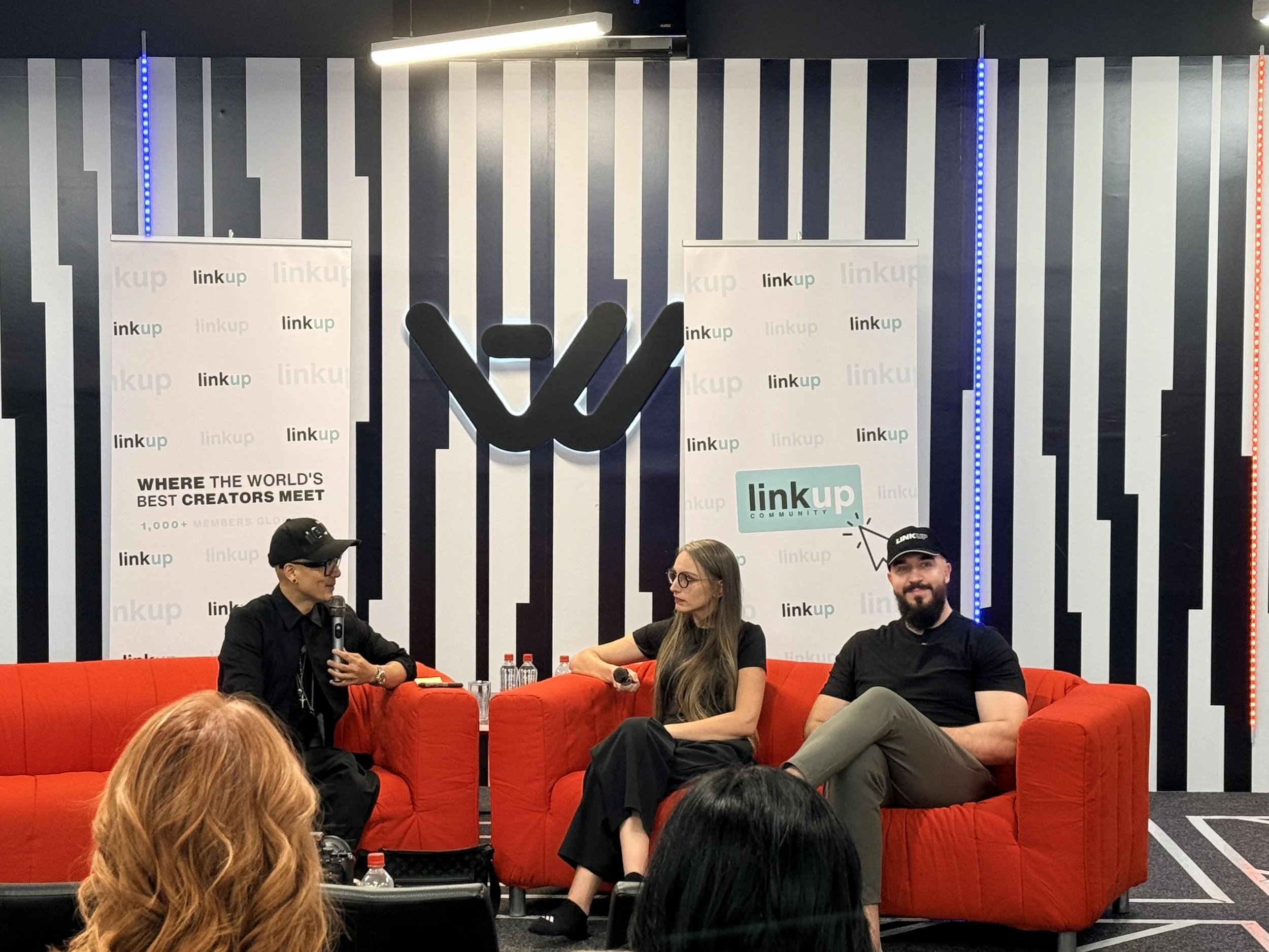 Martina Kikic speaking on stage between personal branding coaches Chris Do and Jasmin Alić at a Link Up Community panel event, seated on orange armchairs in front of a Link Up branded backdrop.