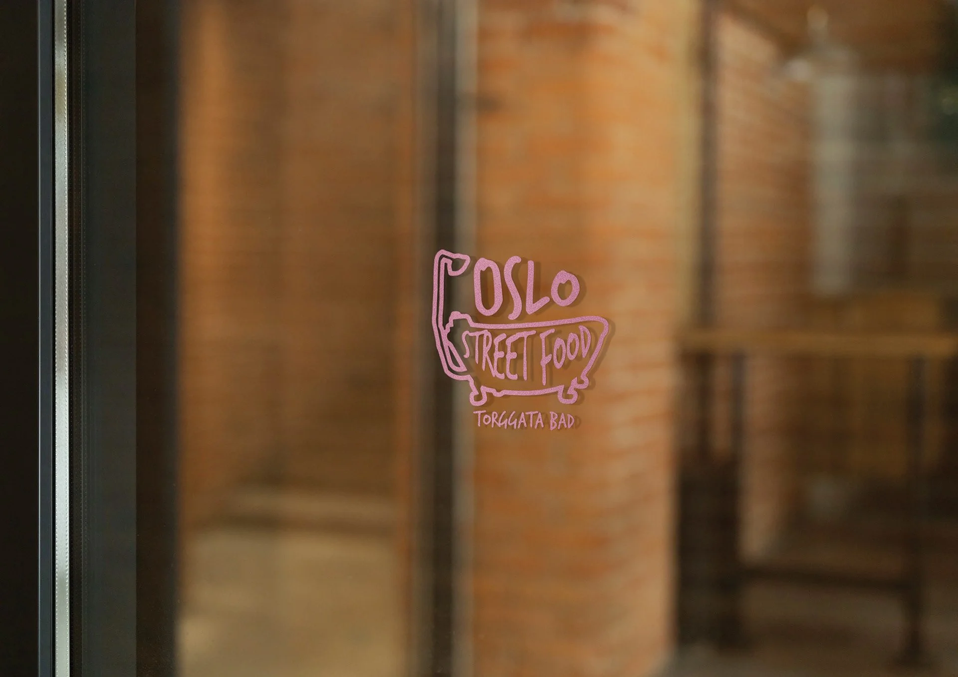 Close-up of a sticker on a glass door with a pink drawing of a bathtub and the words 'Oslo Street Food' and 'Torggata Bad' written inside the tub.