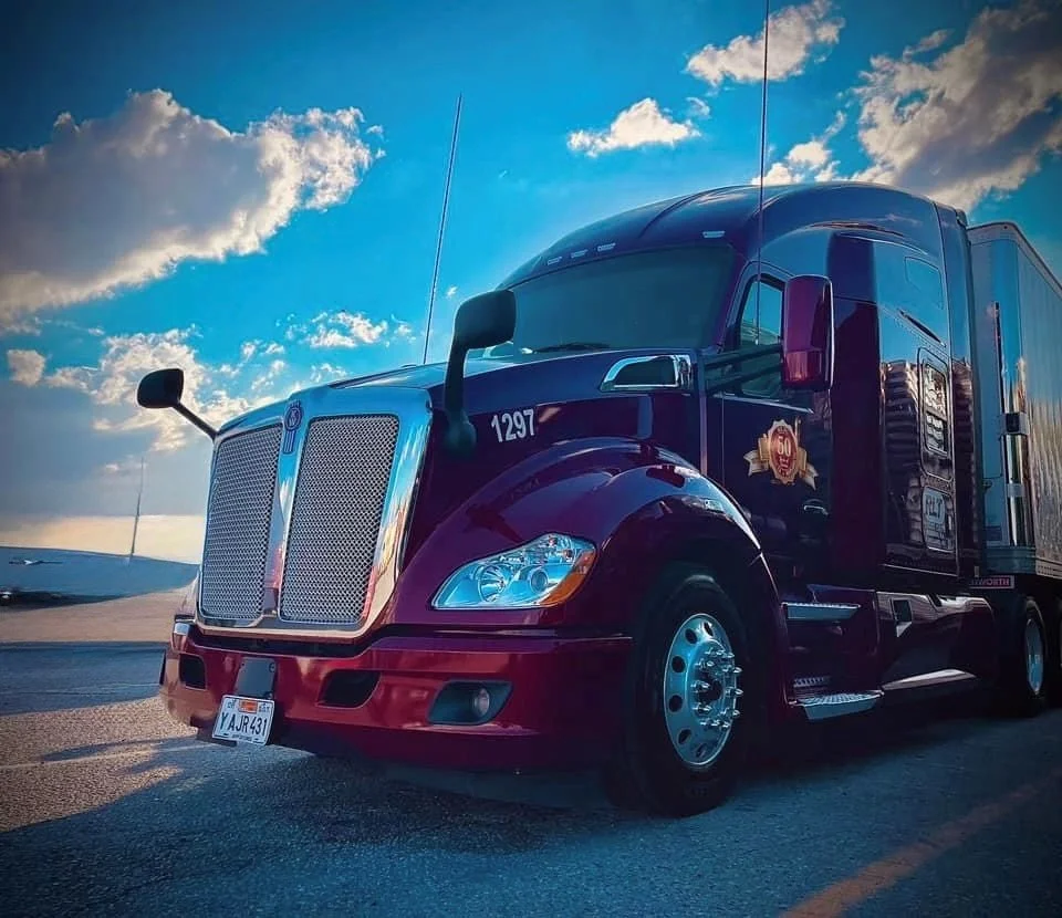 A semi-truck parked on a highway during sunset with cloudy sky in the background.
