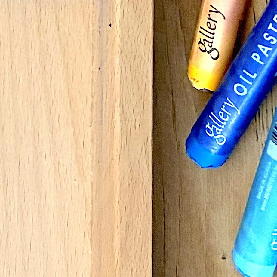 Close-up of oil pastels beside a wooden canvas.
