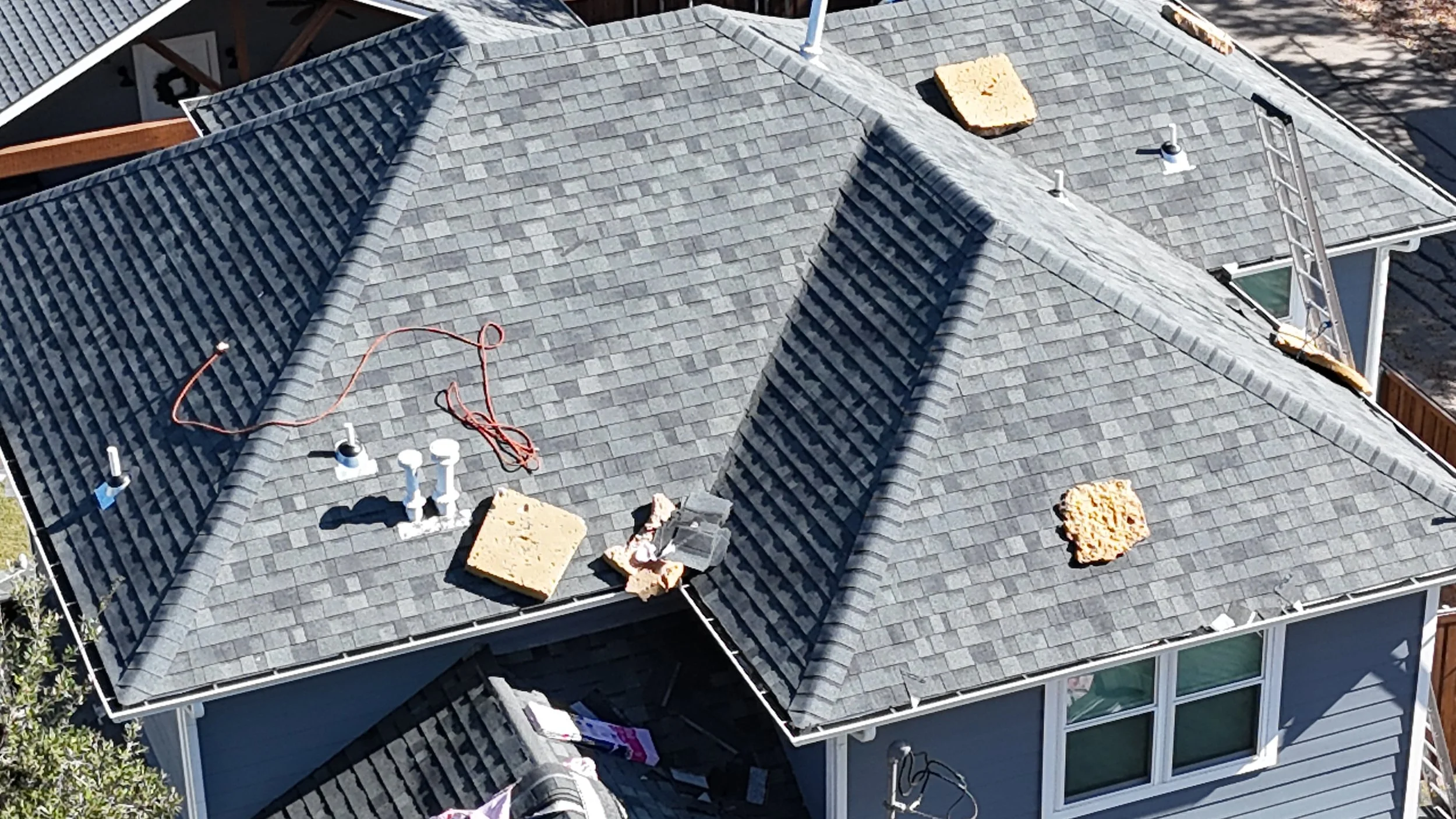Bird's eye view of a gray shingled house roof under construction with tools, insulation foam, and vents visible.