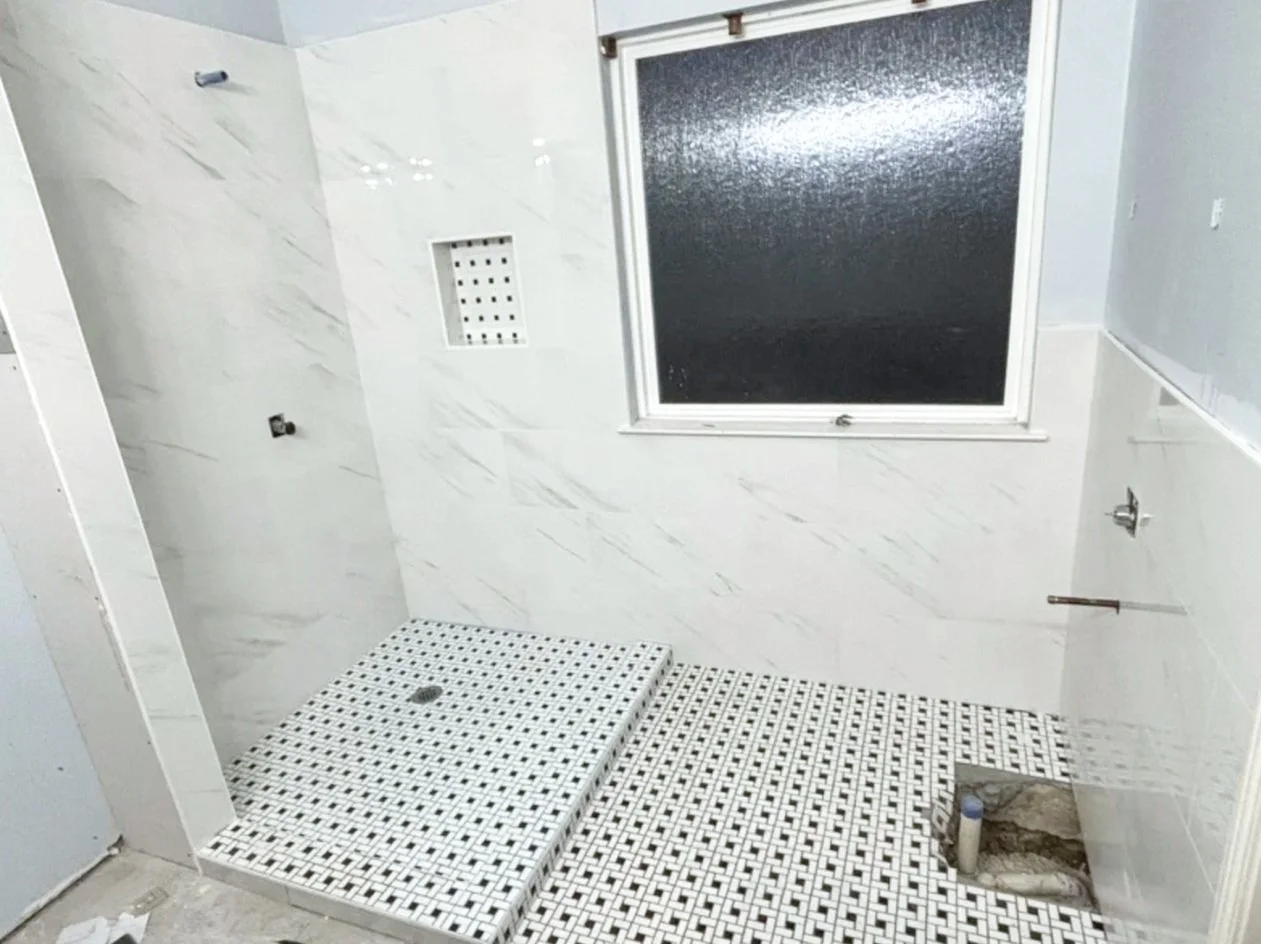 Bathroom or shower area under construction with a tiled floor and wall, a window, and plumbing fixtures.