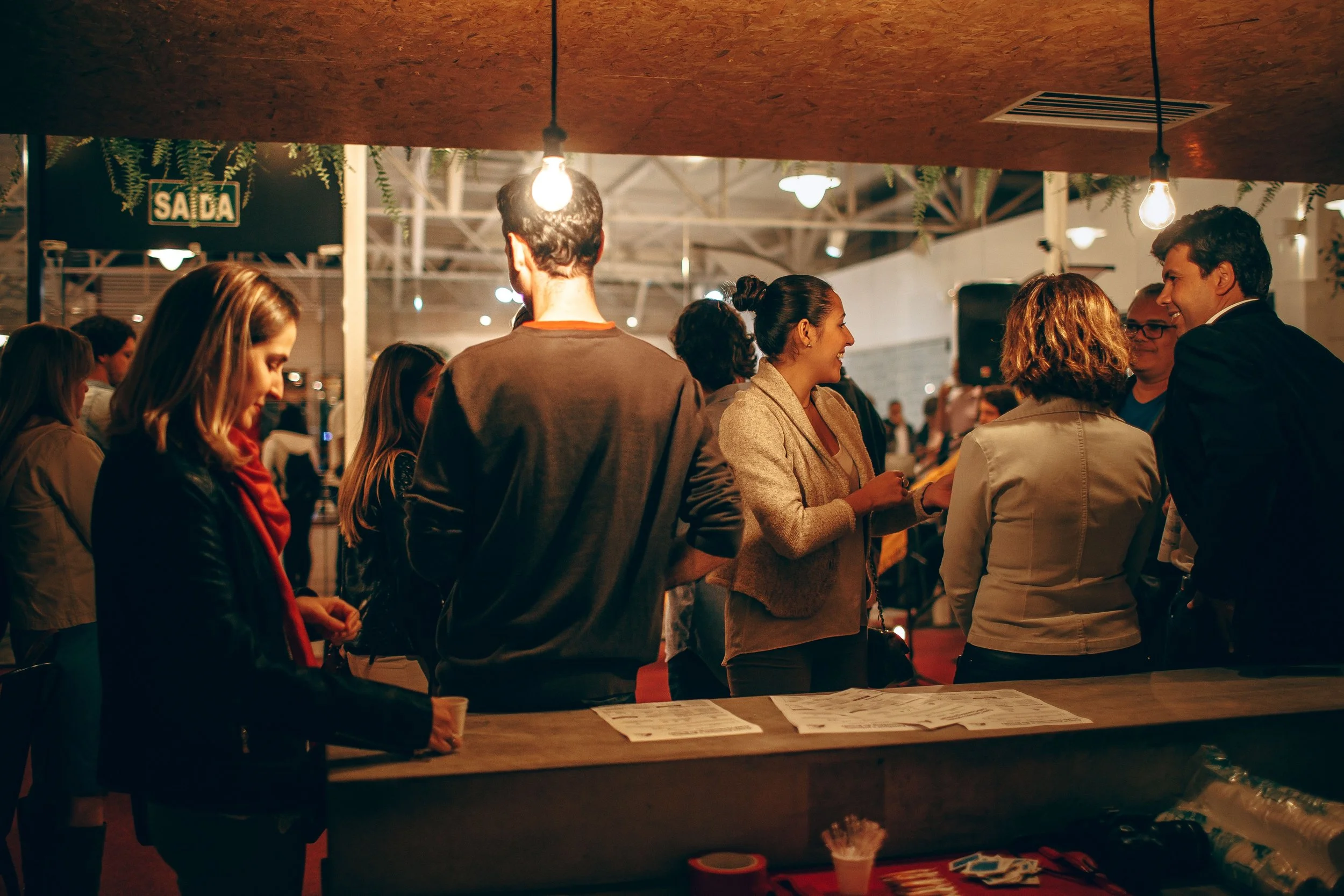 Hombre y mujer conversando sonrientes en evento social, ambiente iluminado, con mesas y ambiente de reuniones.