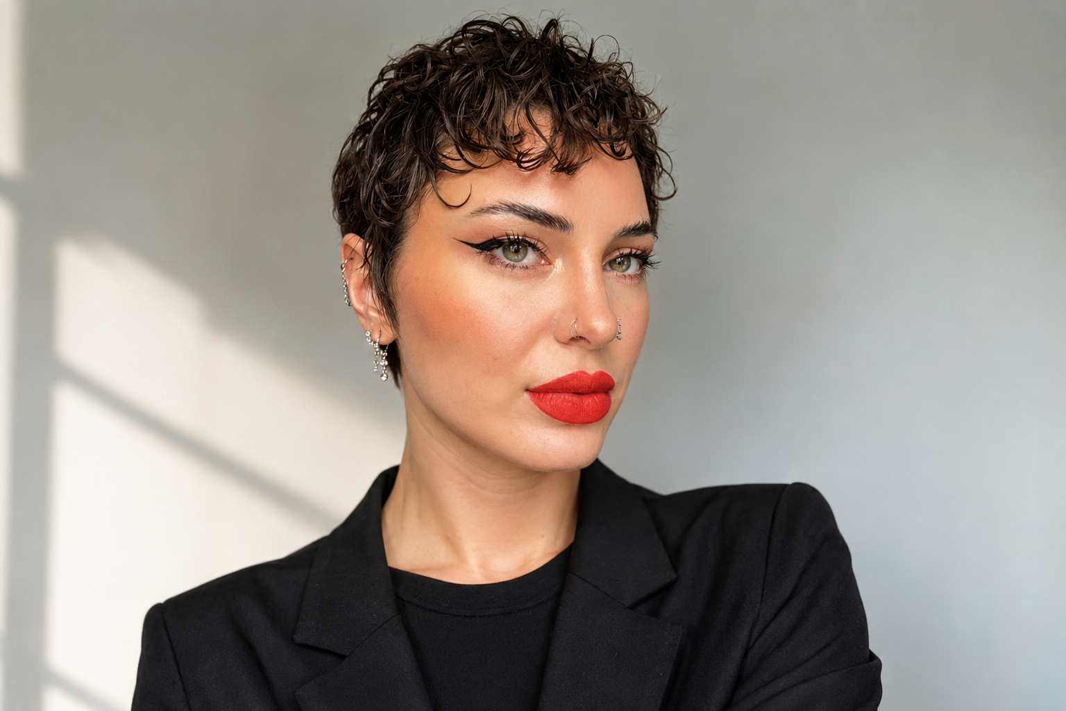 Nahaufnahme eines jungen Frau mit kurzen, lockigen Haaren, rotem Lippenstift, schwarzen Oberteil und Ohrringen, die direkt in die Kamera schaut.