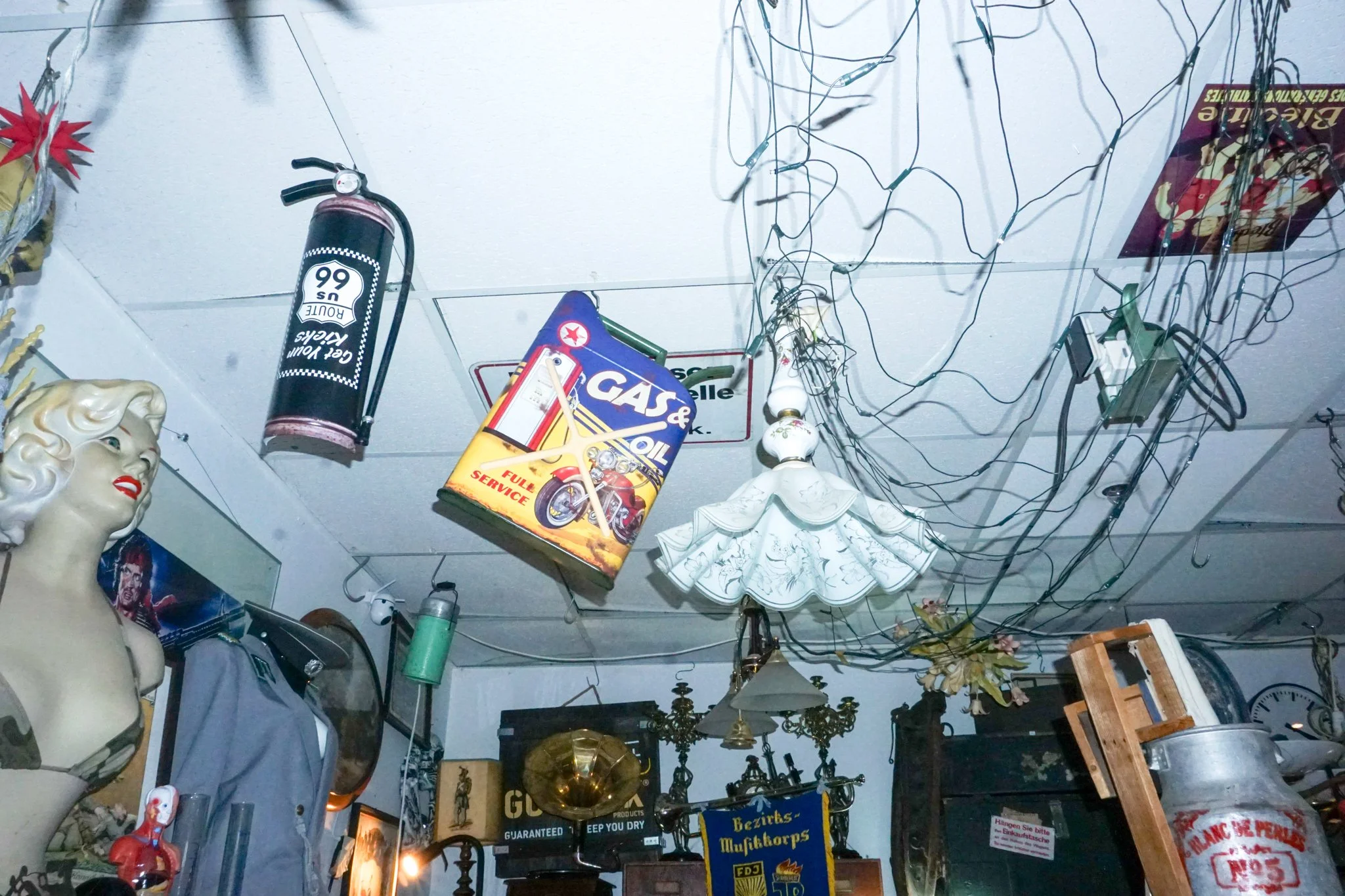 Ein totaler Blick auf eine Raumdecke, die mit verschiedenen Gegenständen, wie alten Lampen, Schildern, Dekorationen, einer menschlichen Kopf-Replik, elektronischen Kabeln, und verschiedenen dekorativen Gegenständen gefüllt ist.