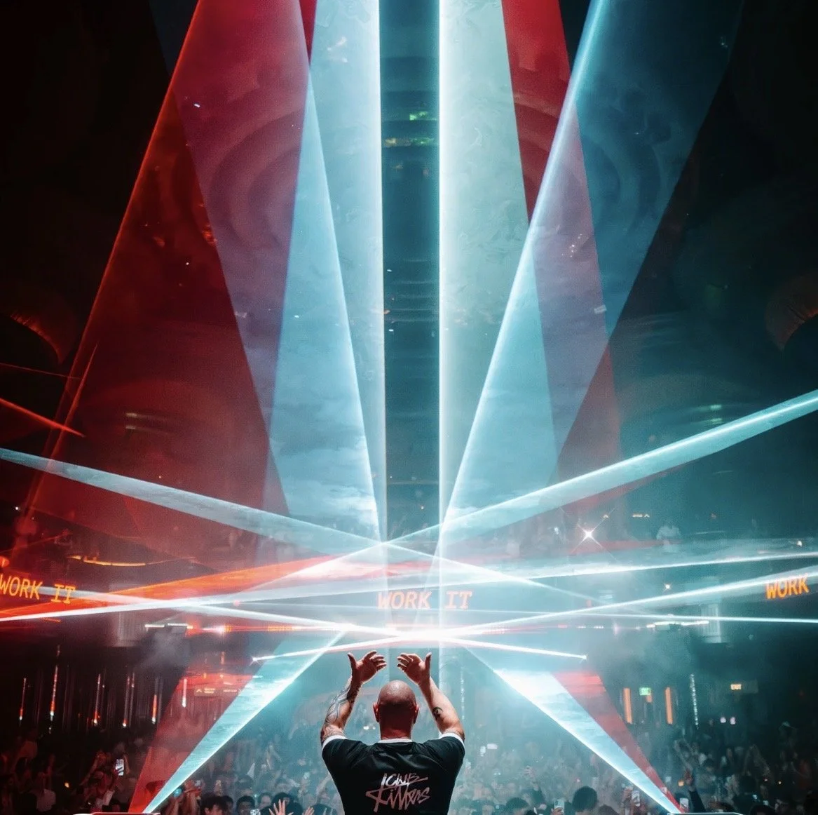 A DJ performs at a nightclub with colorful laser lights and a crowd dancing.