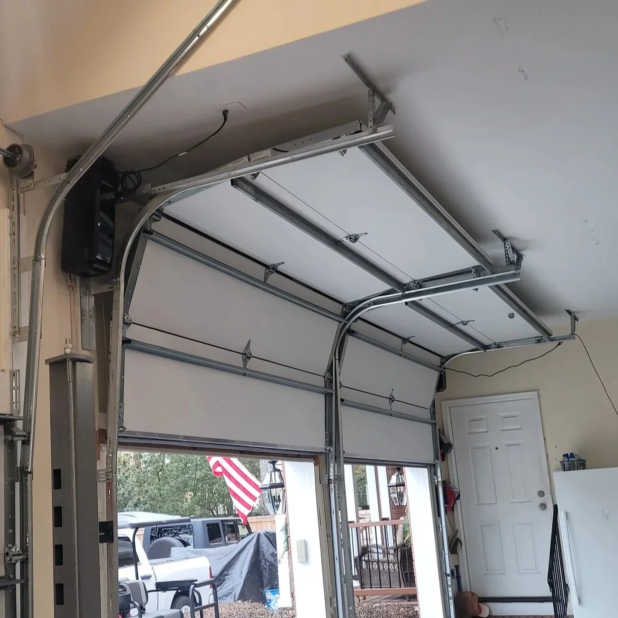 Inside view of a garage with an open automatic overhead door, showing the mechanical and electronic components of the garage door system.