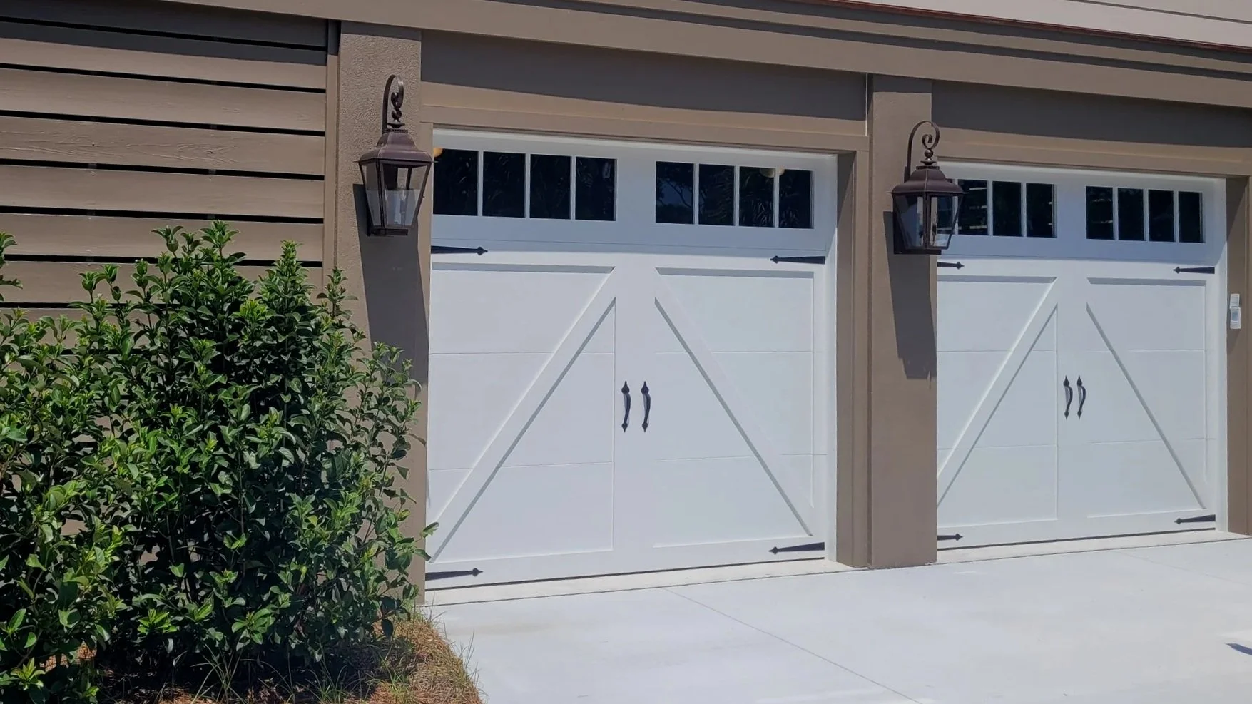 Two white garage doors with black handle pulls, side by side, with a brown exterior wall