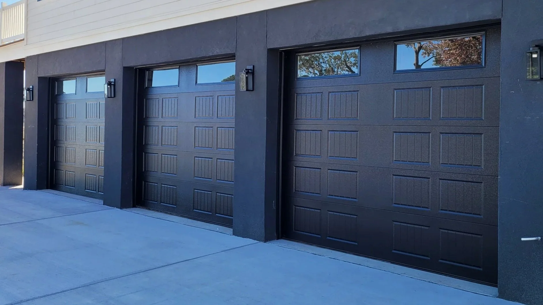 Three black garage doors with windows at the top, mounted on a modern building with black exterior walls