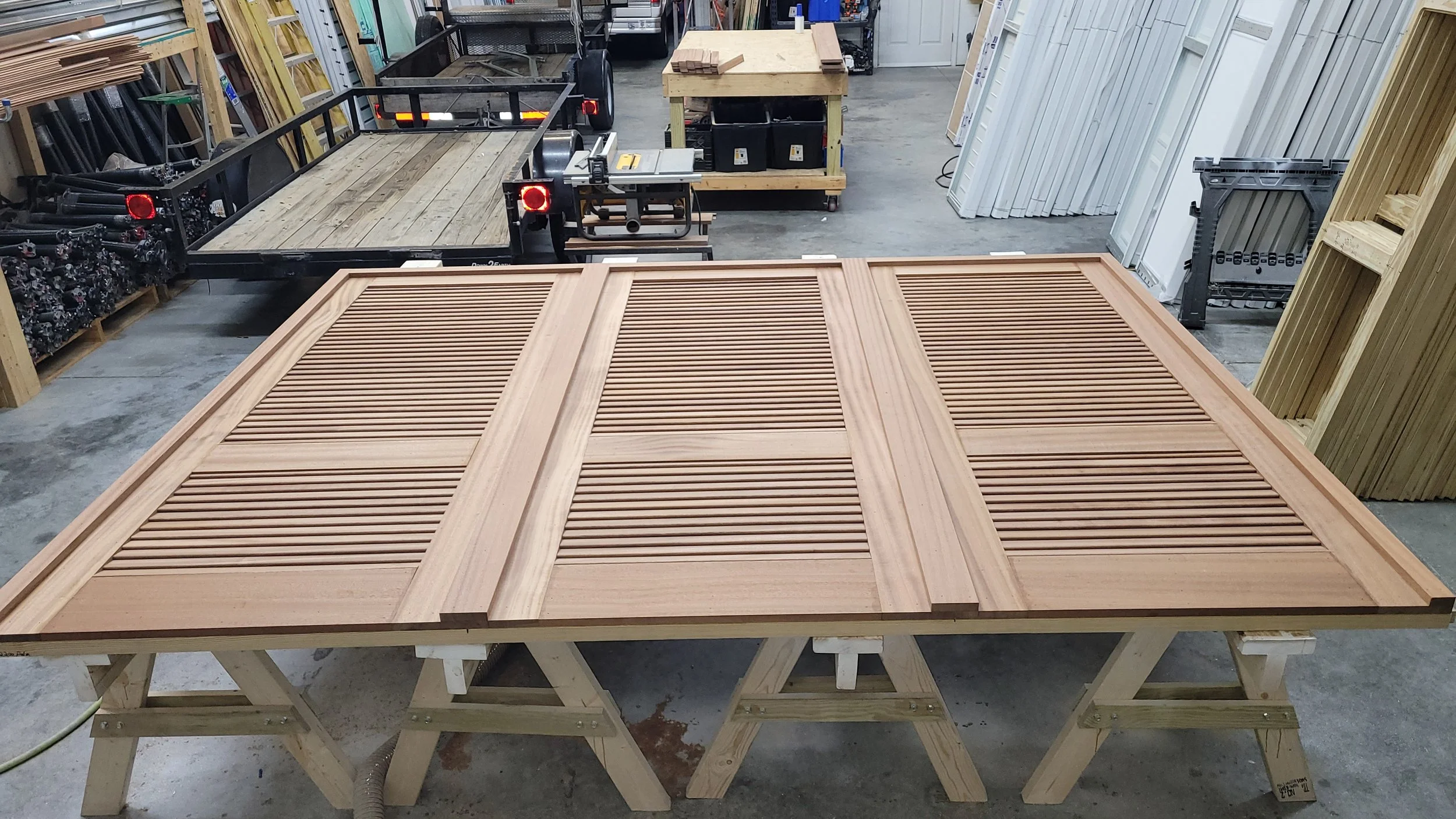 Wooden louvered door or panel in workshop with saws, workbenches, and storage shelves in the background.