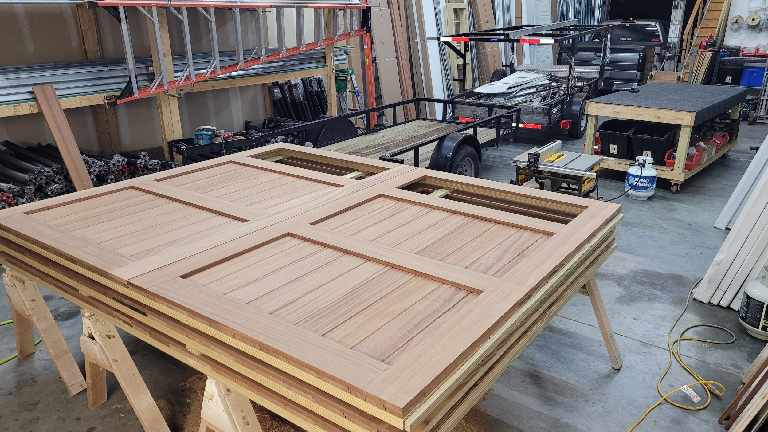 Wooden door panels on workbenches in a woodworking shop with tools and materials around.
