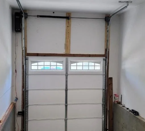 Empty garage with a closed white sectional garage door, unfinished walls, and storage on the right side.