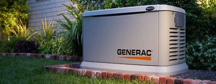 A Generac home backup generator installed in a landscaped yard with grass, plants, and a brick border.