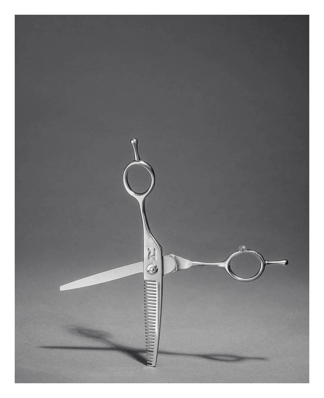 A pair of haircutting scissors shaped like an umbrella, with one blade open and the other closed, against a plain gray background.