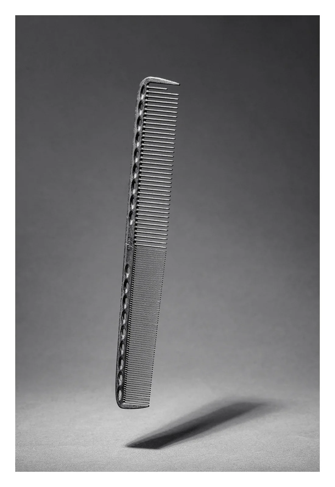 A haircutting comb standing vertically on a gray surface with a shadow cast beneath it.