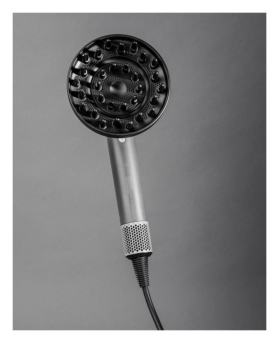 A modern, black and silver hairdryer with a round, vented drying head against a gray background.