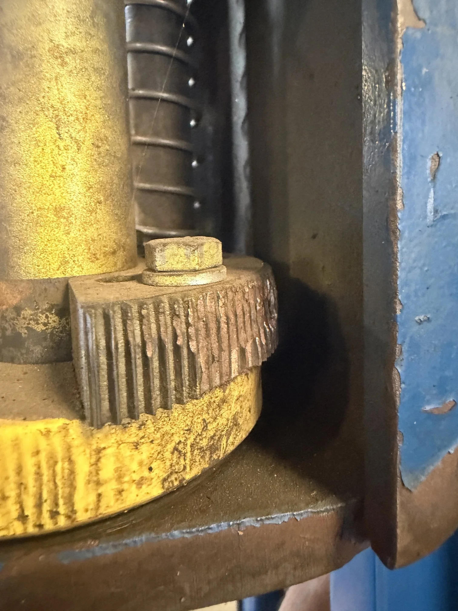 Close-up of a mechanical gear or part in a machine, showing a yellow gear with worn edges, a darker gear or component with teeth, and some black and metallic elements.