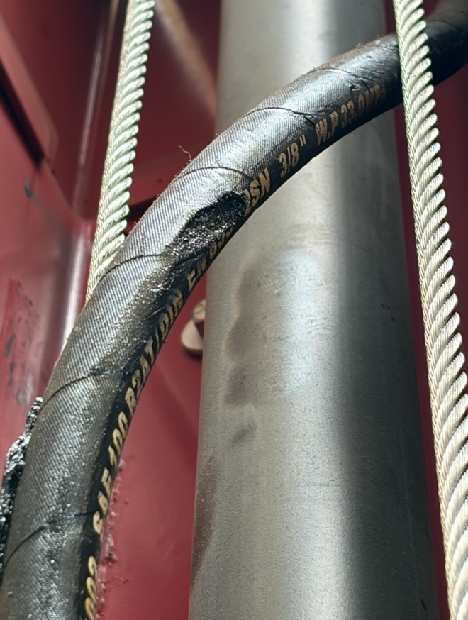 Close-up of worn black and silver electrical cable with yellow text, next to a white rope and a metallic pipe, with a red background.