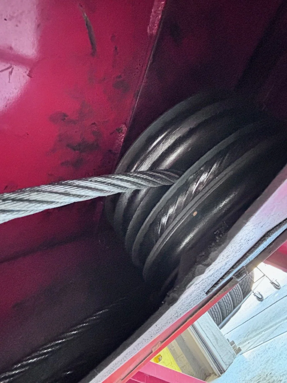 Close-up of a metal cable passing through a sheave or pulley inside a red mechanical or industrial equipment.
