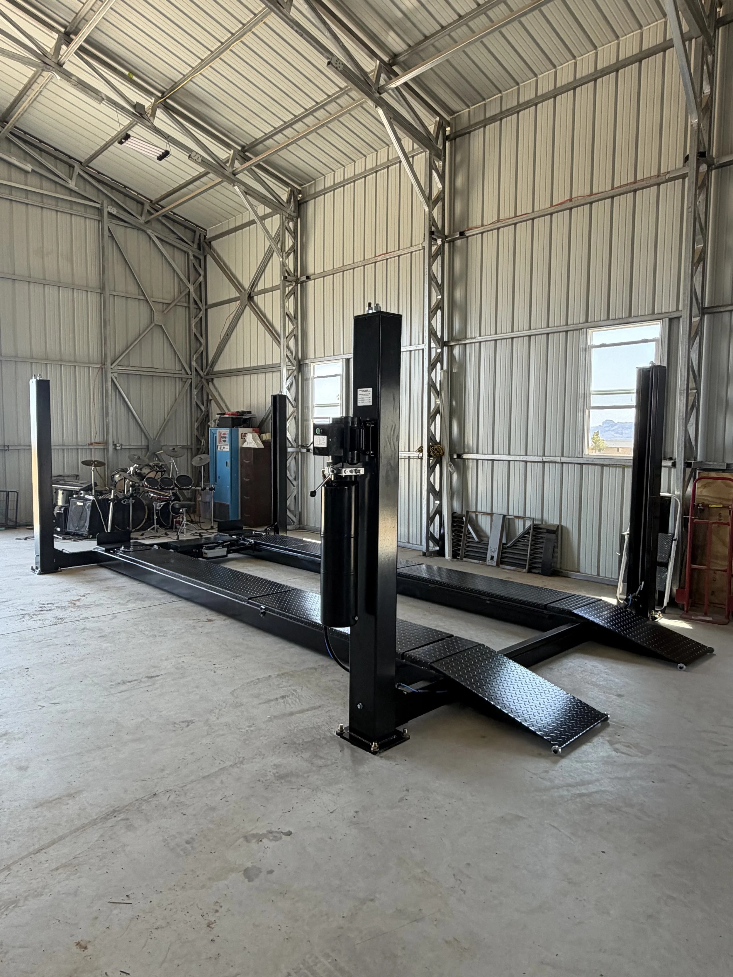 An automotive wheel alignment machine inside an industrial garage with metal walls and windows.