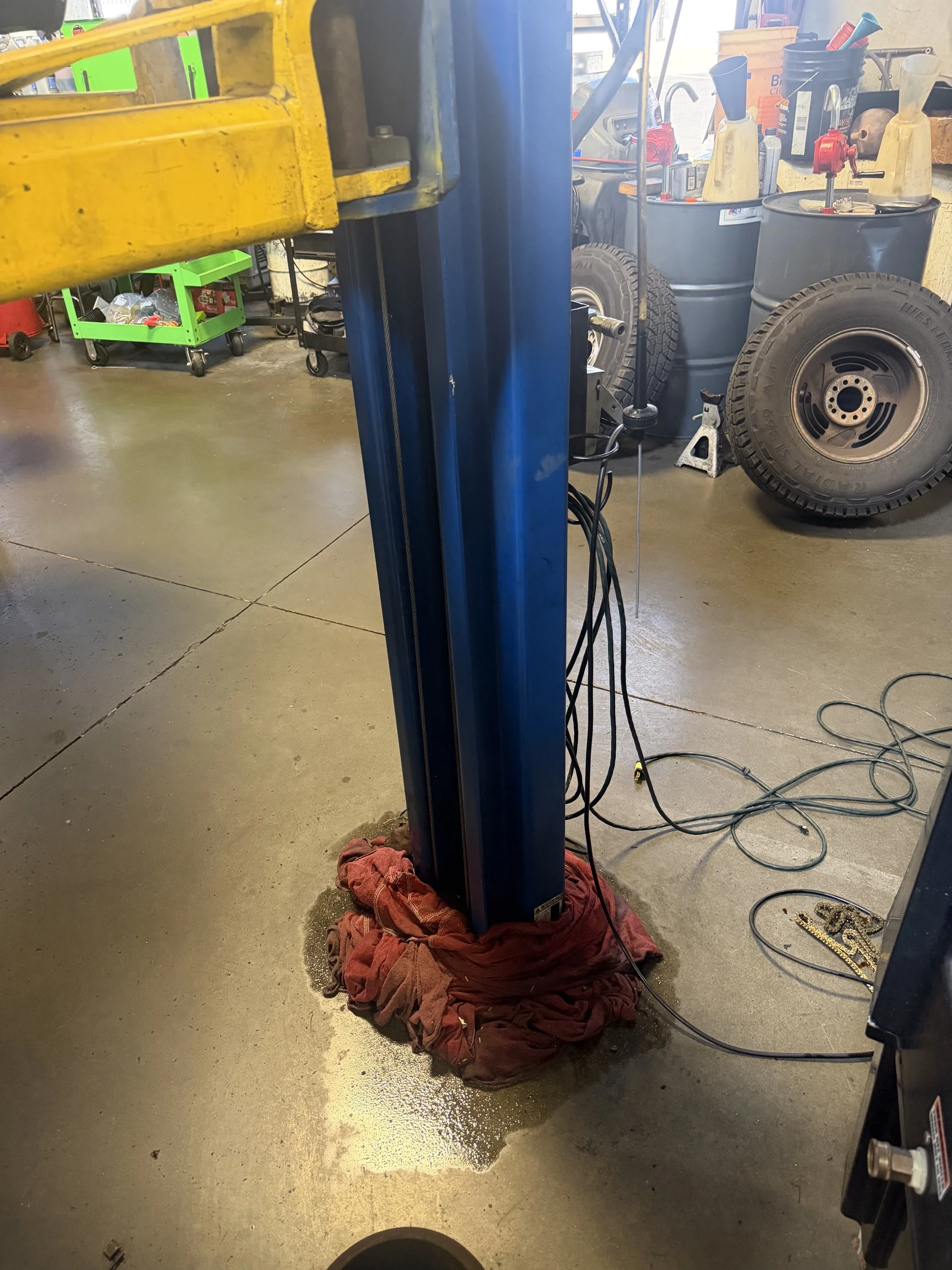 A blue hydraulic lift in a garage or workshop with a red cloth and some spilled liquid on the floor underneath. Lift installer