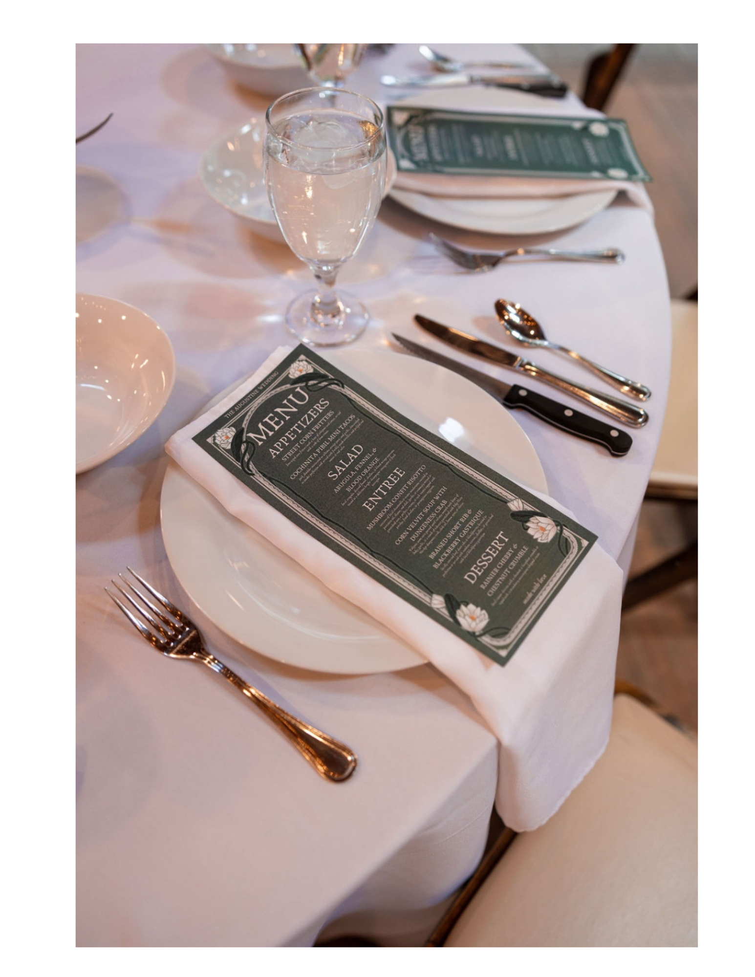 A formal dining table setting with a water glass, cutlery, a menu on a white napkin, and a white tablecloth. The menu reads 'Appetizers,' 'Salad,' 'Entree,' and 'Dessert'.