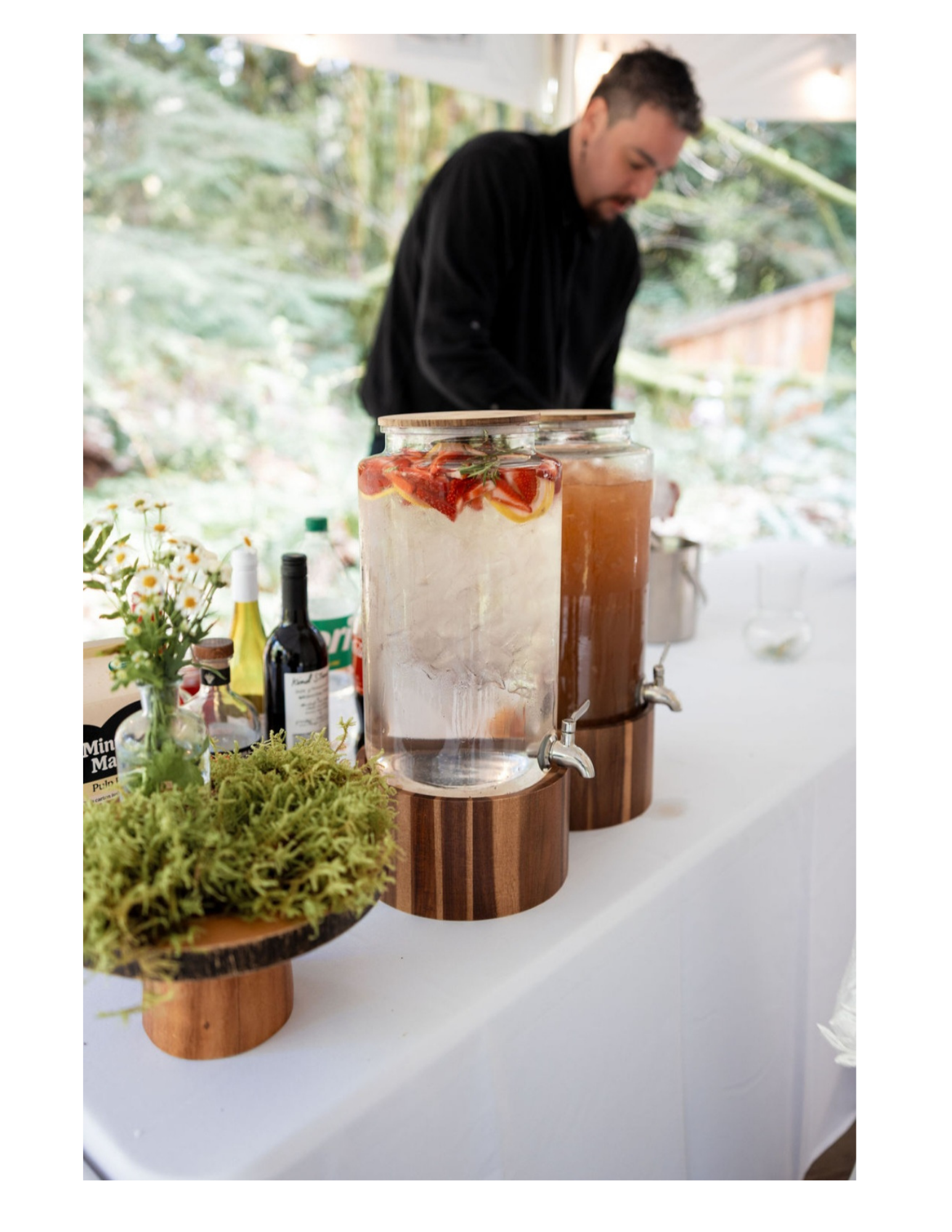 a man serving drinks at a bar with plant decorations and water pitchers