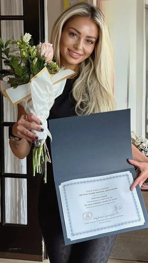 Cristina Ponzio celebrating her 200-hour yoga teacher training graduation while holding flowers and her certification.