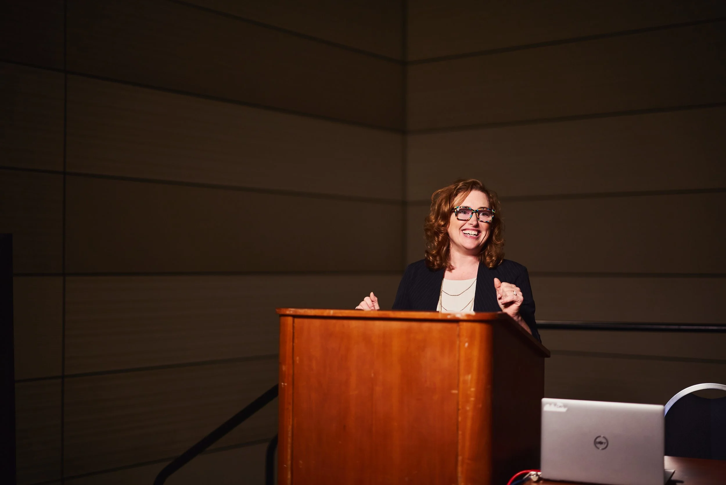 Dr. Melanie Barham is smiling while standing behind a wooden podium in a conference room.