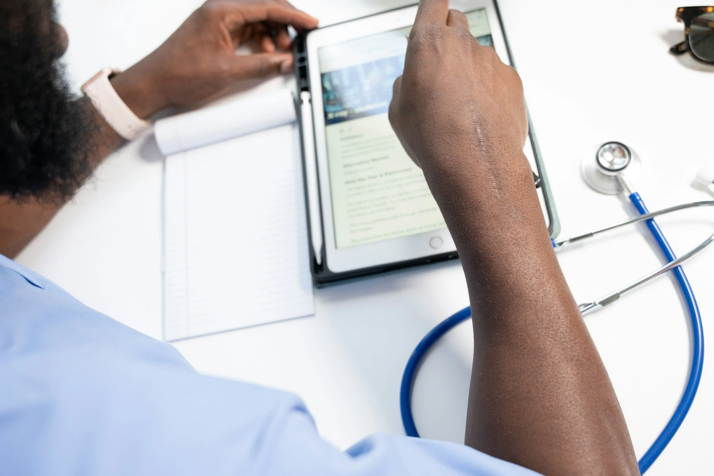 A healthcare professional is examining a tablet displaying medical information, with a stethoscope and medical notes on a white surface.