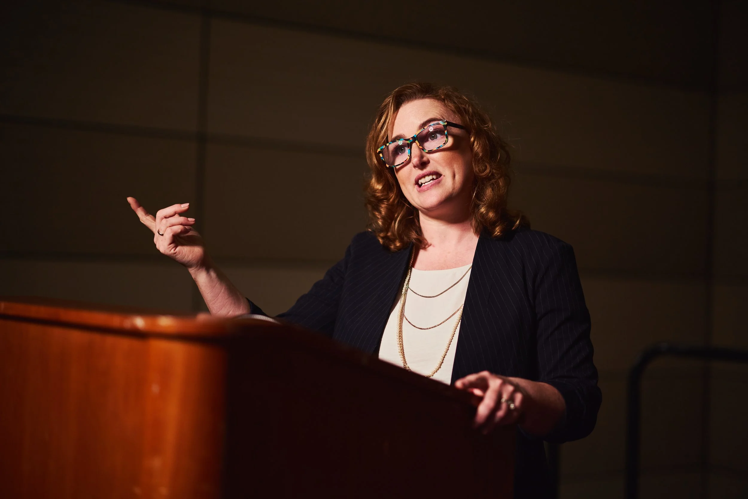 Dr. Melanie Barham is speaking at a podium in a dimly lit room.