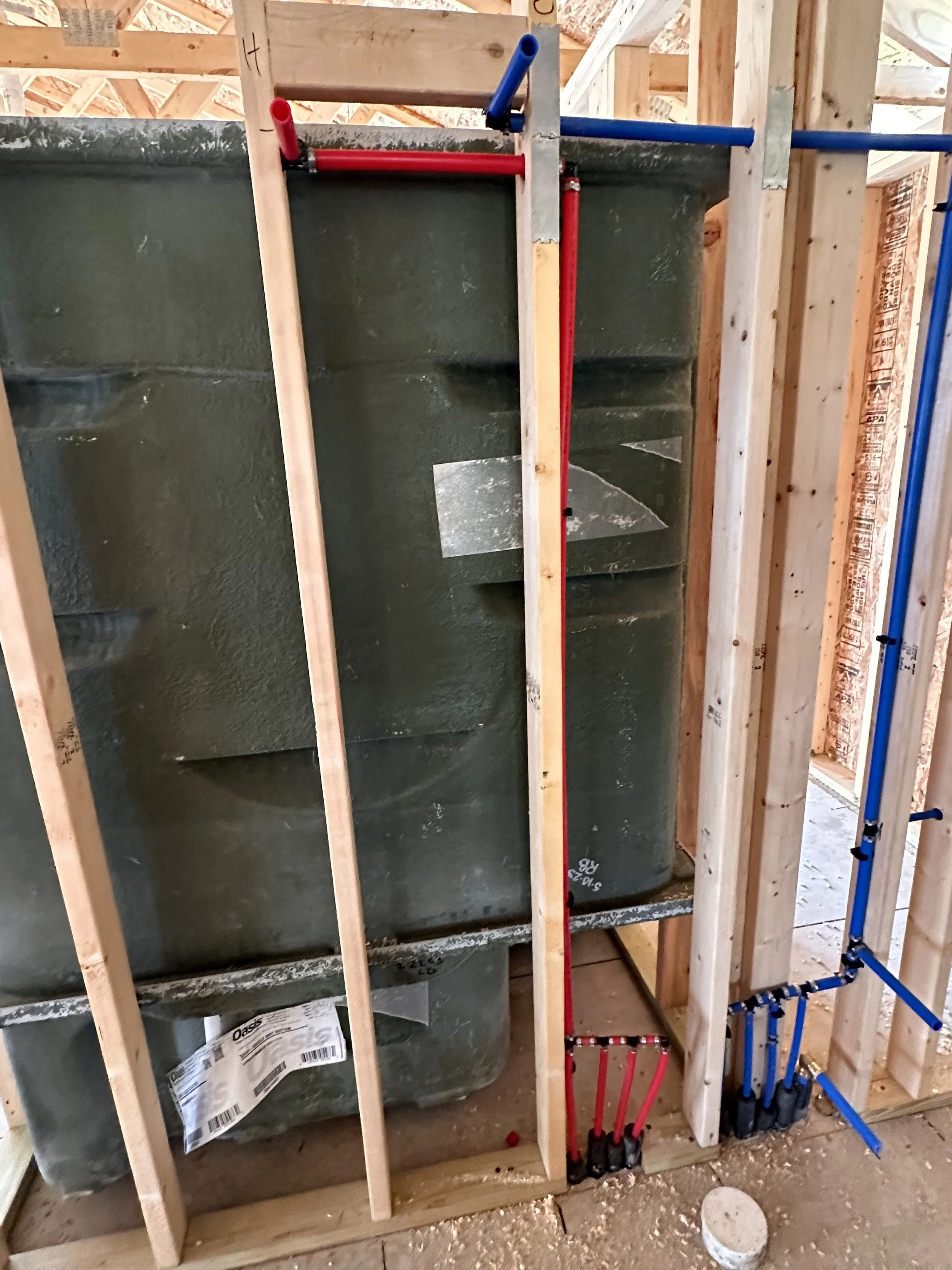 View of water heater in a framed wall structure under construction, with red and blue PEX plumbing pipes and wooden studs.