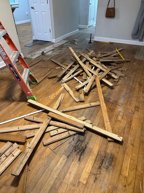 Desorden en una sala con madera rota y herramientas, evidenciando una reparación o demolición en proceso.