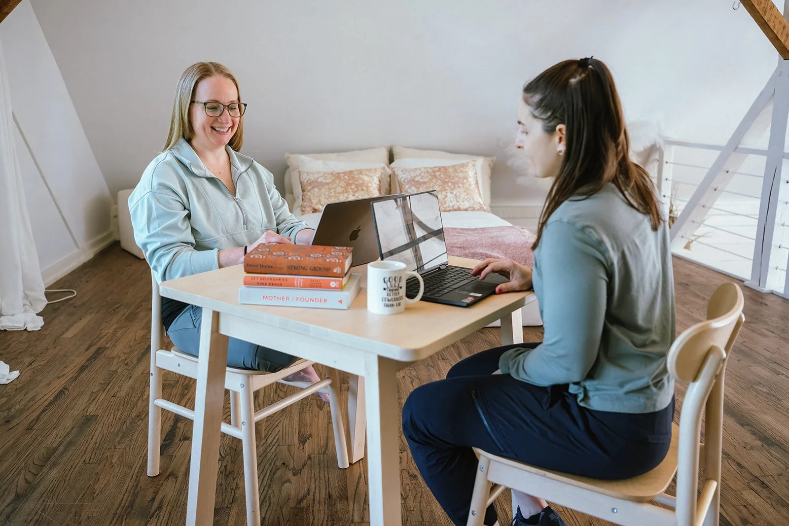Dr Amanda and her healthcare business consulting client at table with laptops and books in a cozy room.
