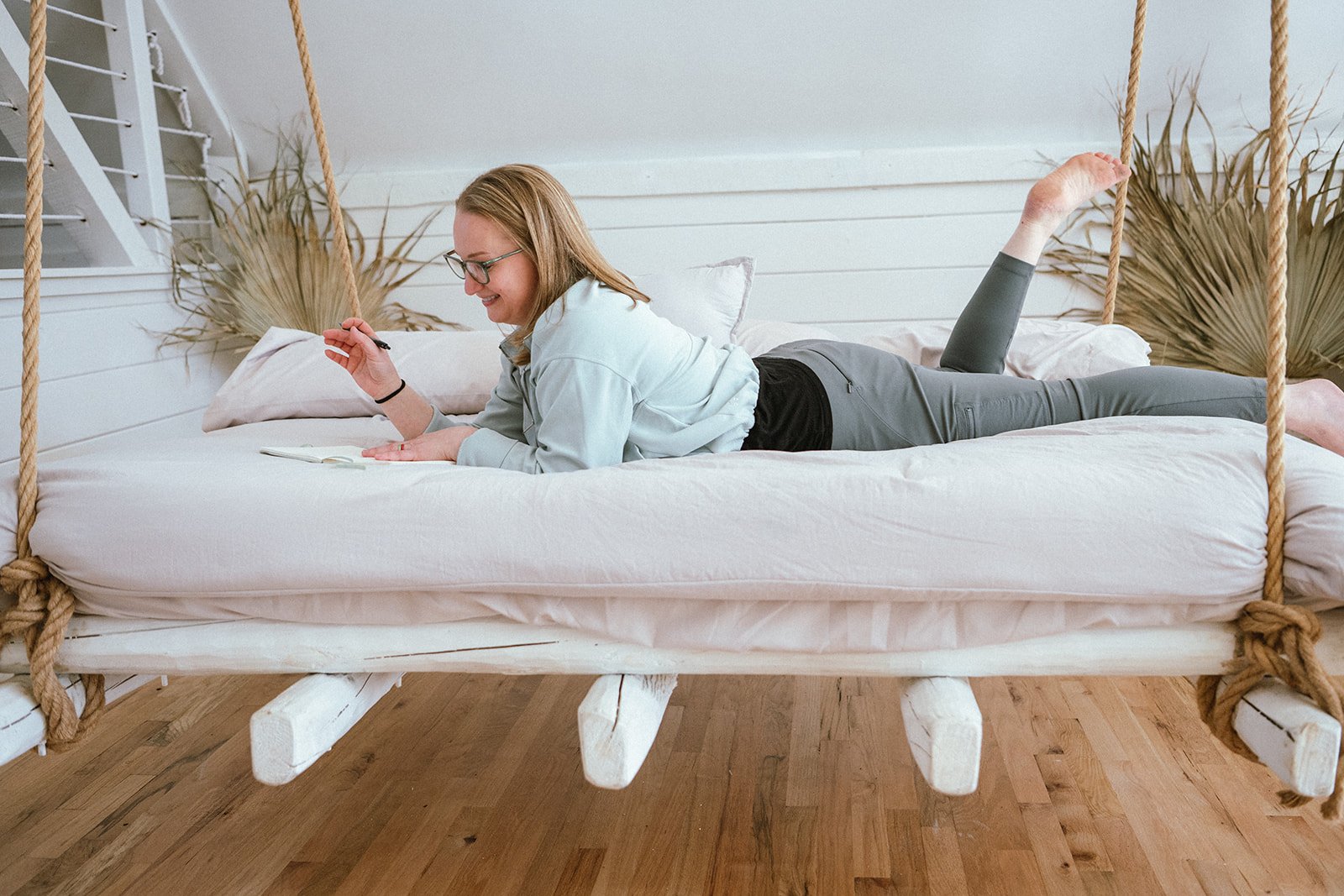 Amanda Townsnd journaling with a smile, in a bedroom with white shiplap walls and dried palm leaves decor.