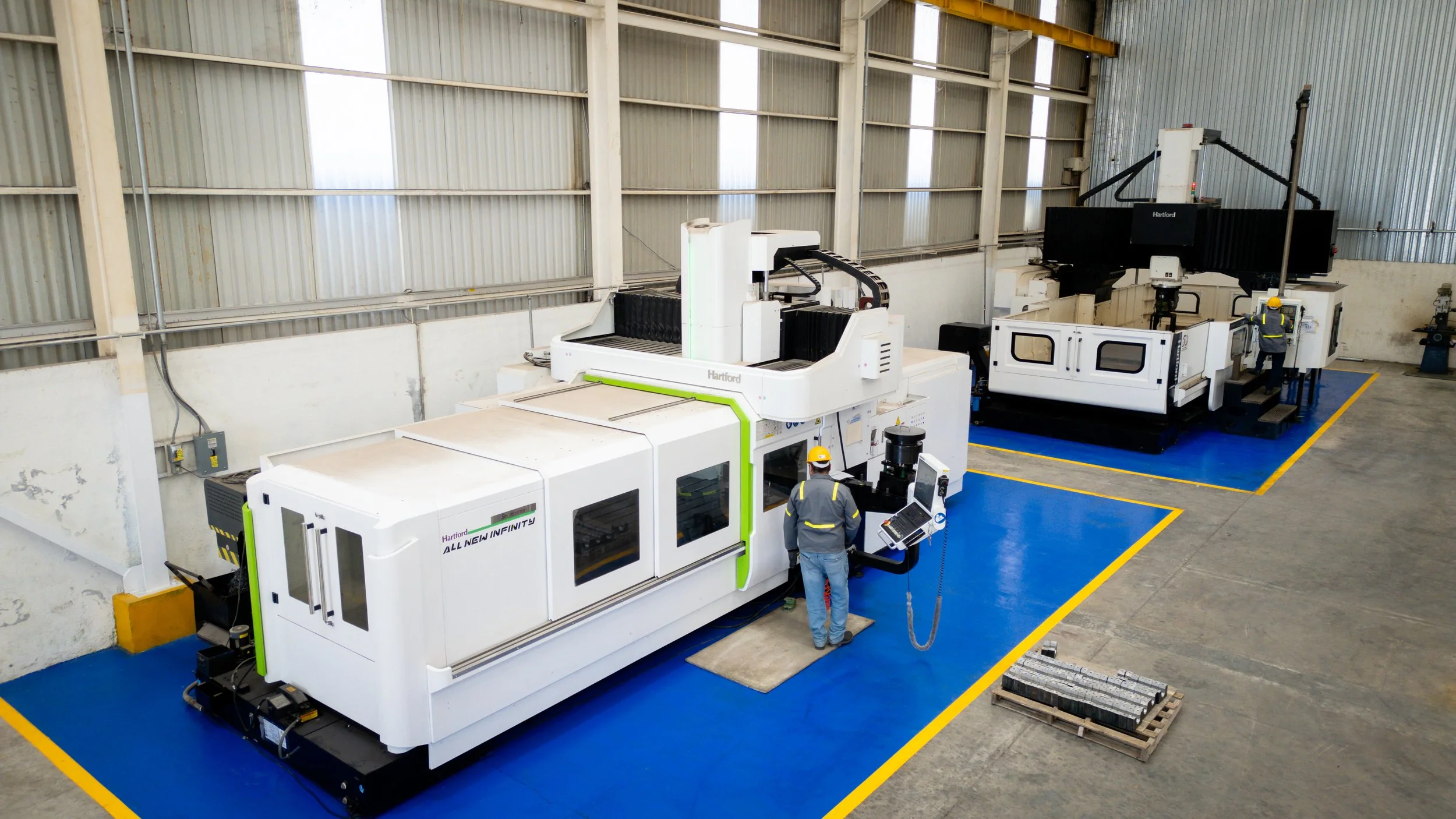 Máquinas de manufactura industriales en un almacén, con trabajadores operando y supervisando los equipos.