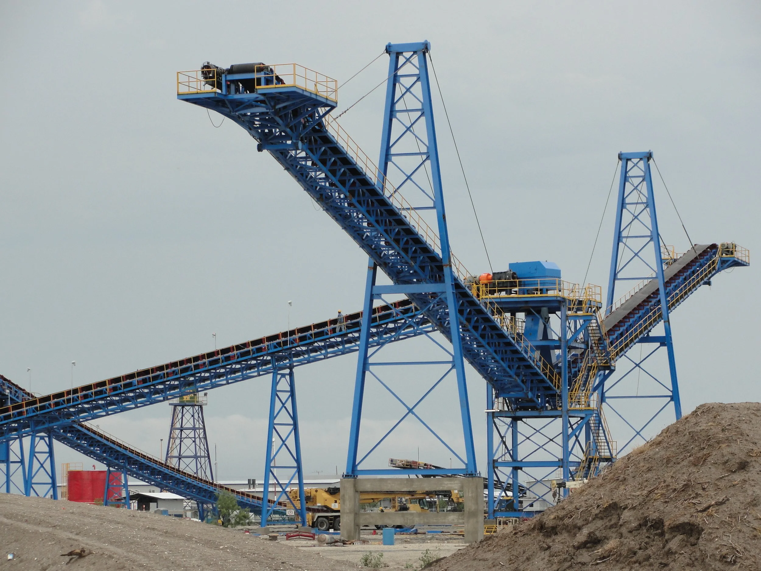 Estructura azul de una montaña rusa en construcción con plataformas y caminos elevados, sobre un terreno de tierra en un día nublado.