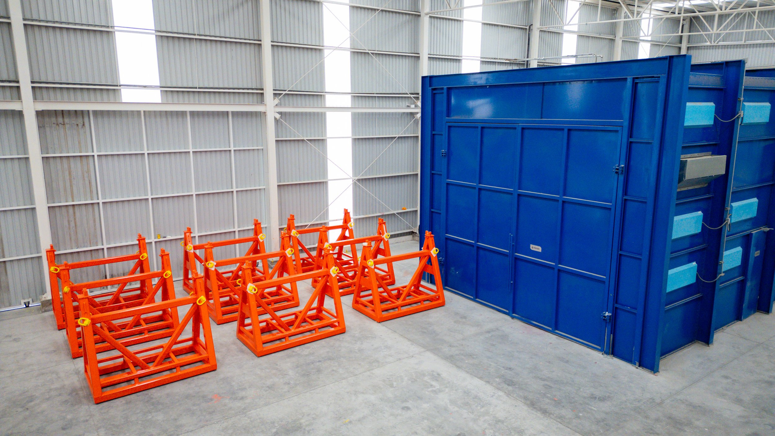 Interior de una nave industrial con estructuras de metal y paredes de lámina. Hay varias bases de color naranja y una estructura grande azul para almacenamiento o maquinaria.