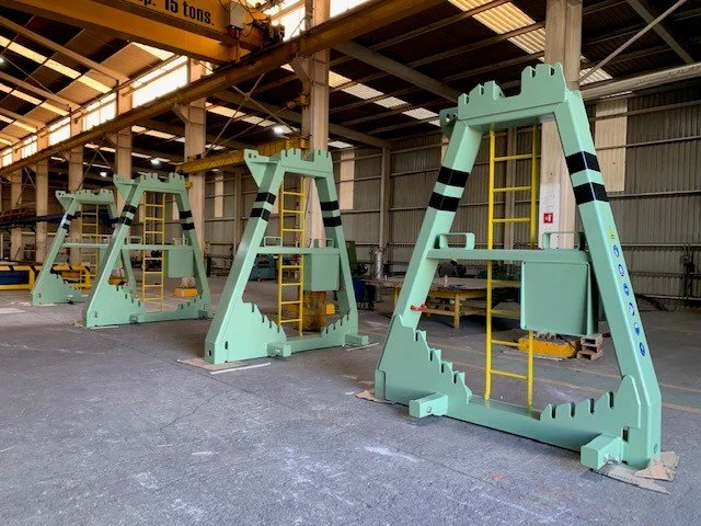Tres grandes estructuras metálicas verdes en un taller, parecen ser equipos de entrenamiento o maquinaria industrial.