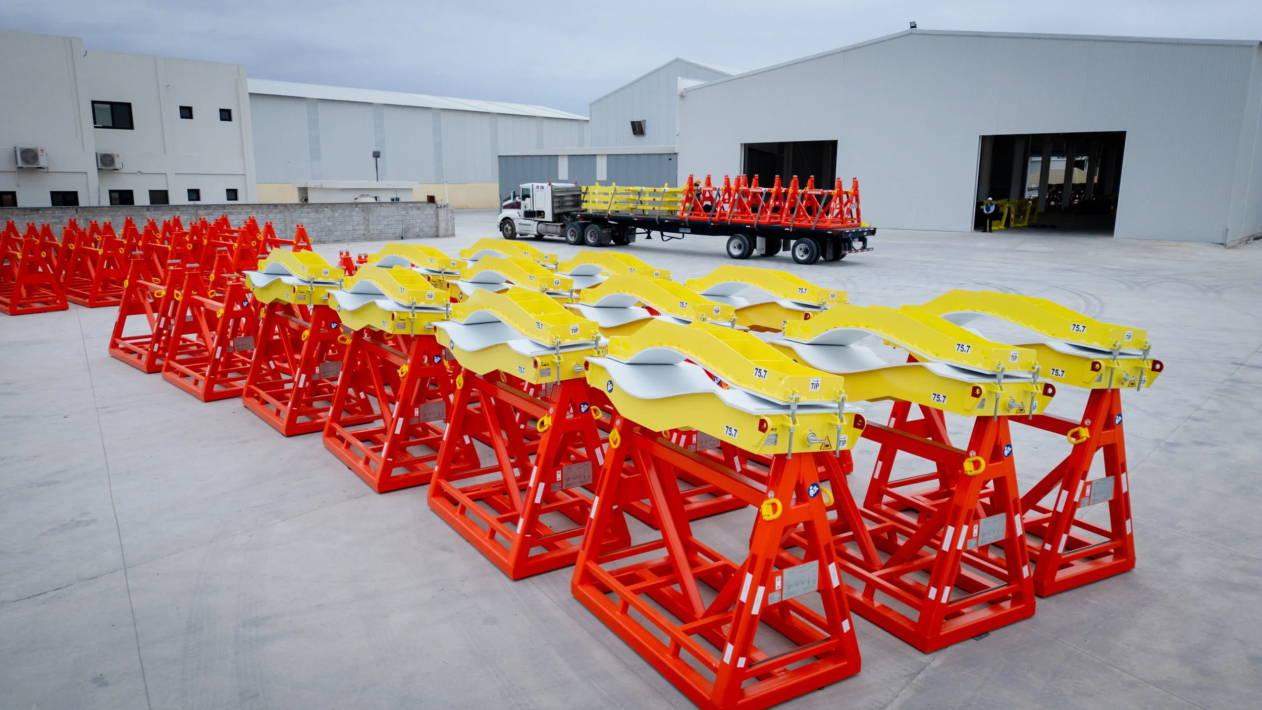 Lotes de señalización de trabajo en color amarillo y naranja en un área de aparcamiento industrial. Cerca de un camión con plataforma para transporte de señalización.