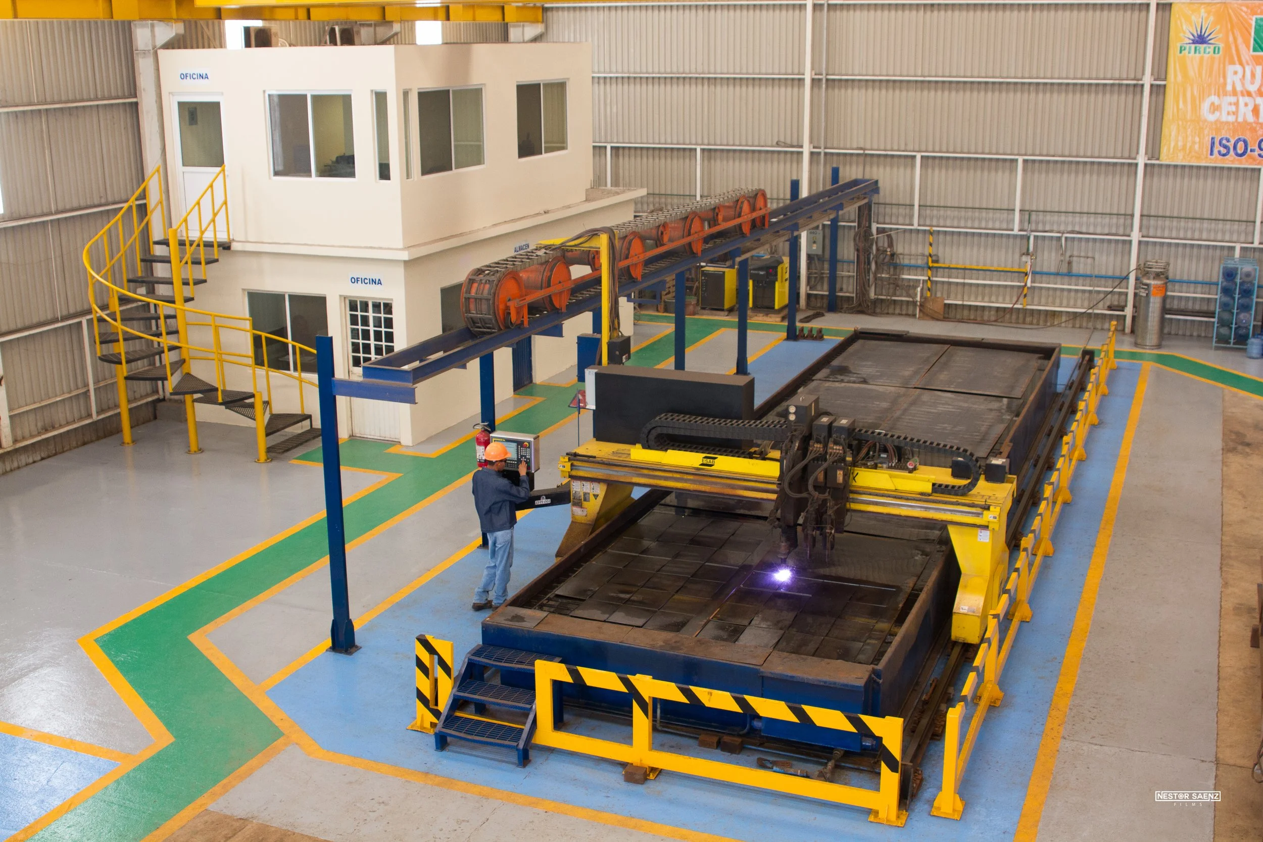Imágenes de una planta industrial con maquinaria de mecanizado. Una persona con casco de seguridad y uniforme de trabajo está operando un control en una máquina grande de fabricación.
