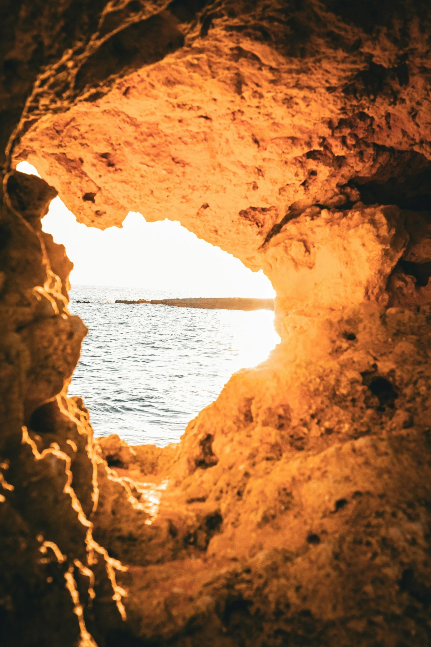 View of the ocean through a rocky cave opening during sunset.