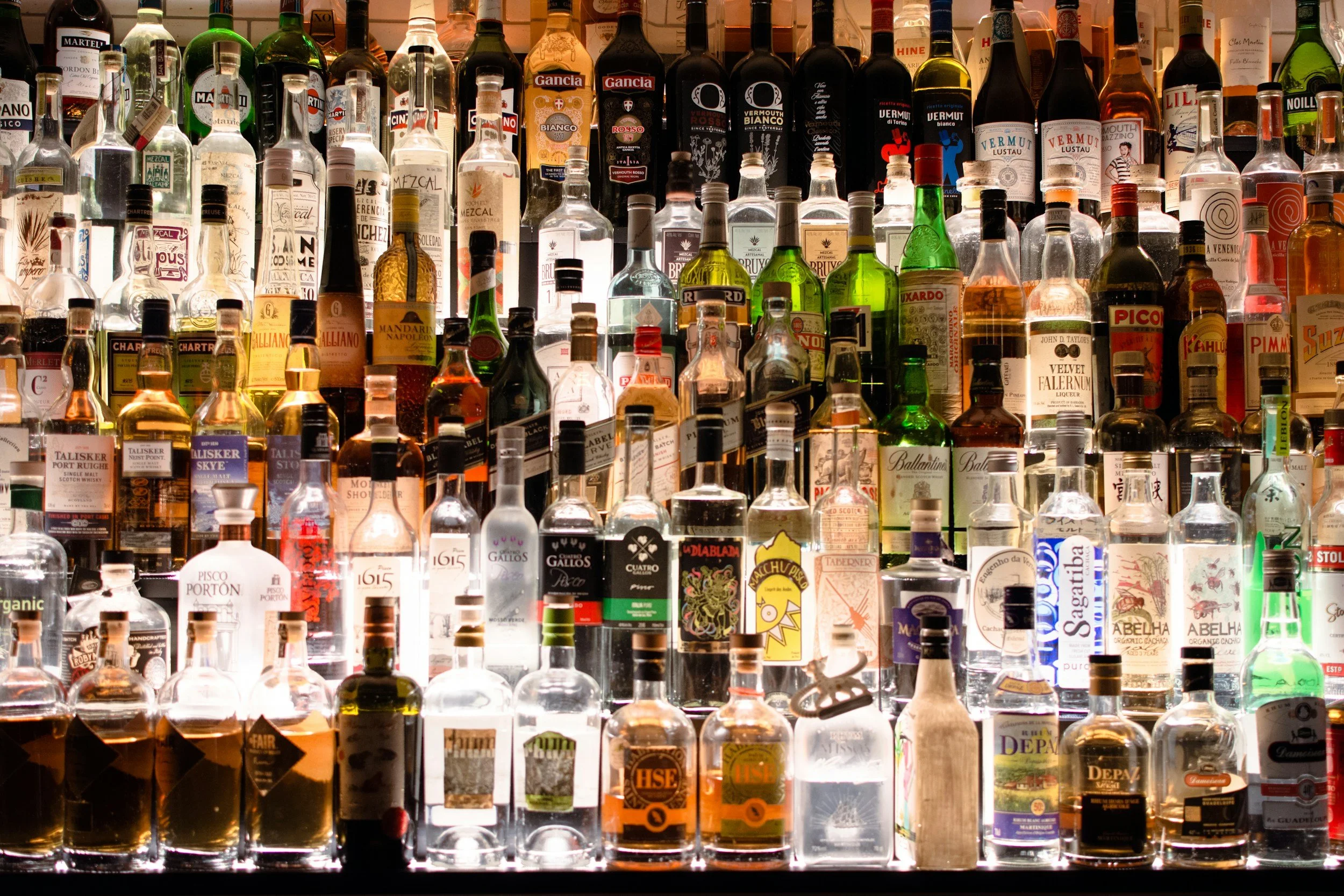Photo of many many assorted alcohol bottles lit from behind and below